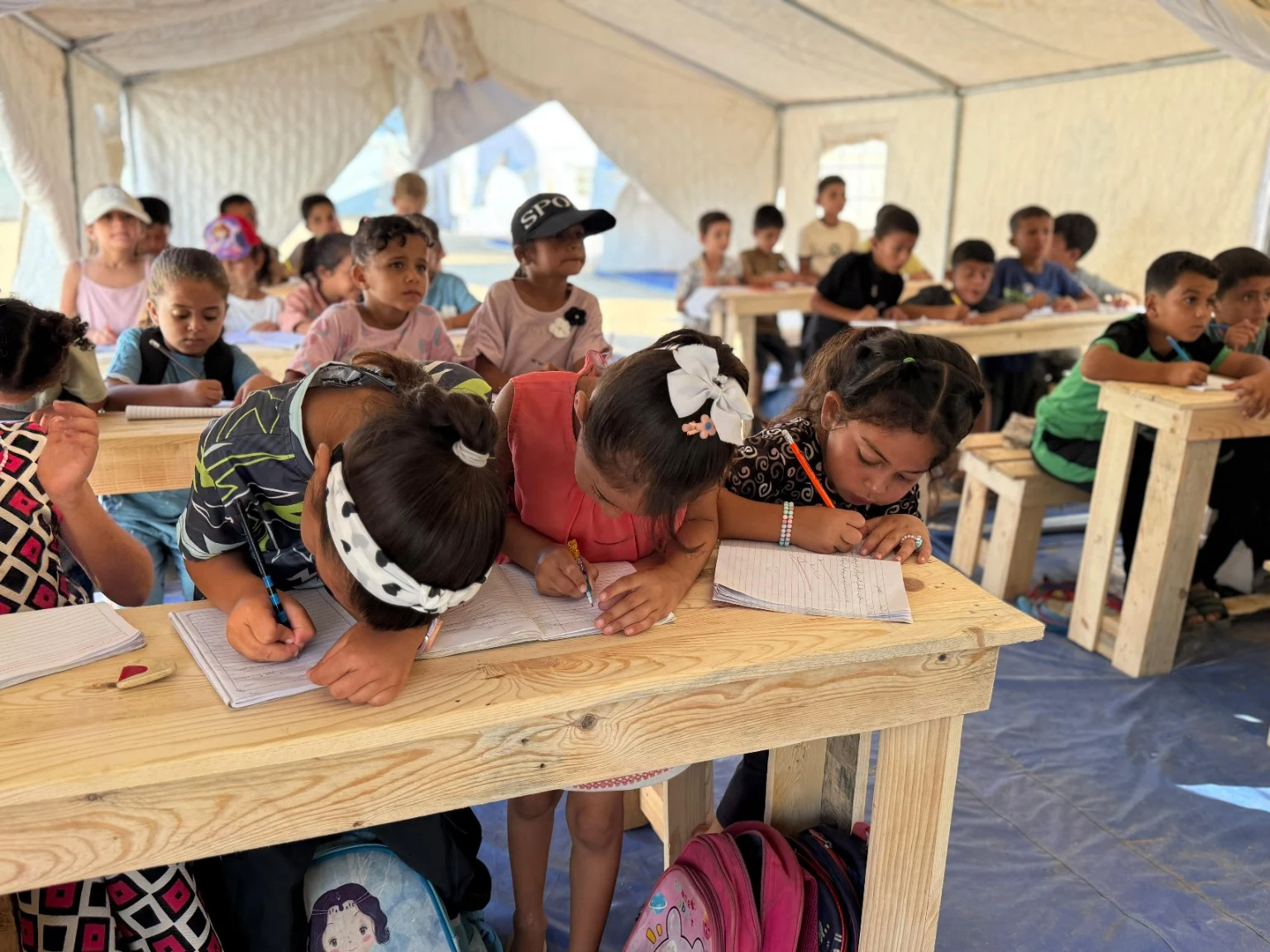 Des enfants écrivent dans leurs cahiers dans une salle de classe sous tente