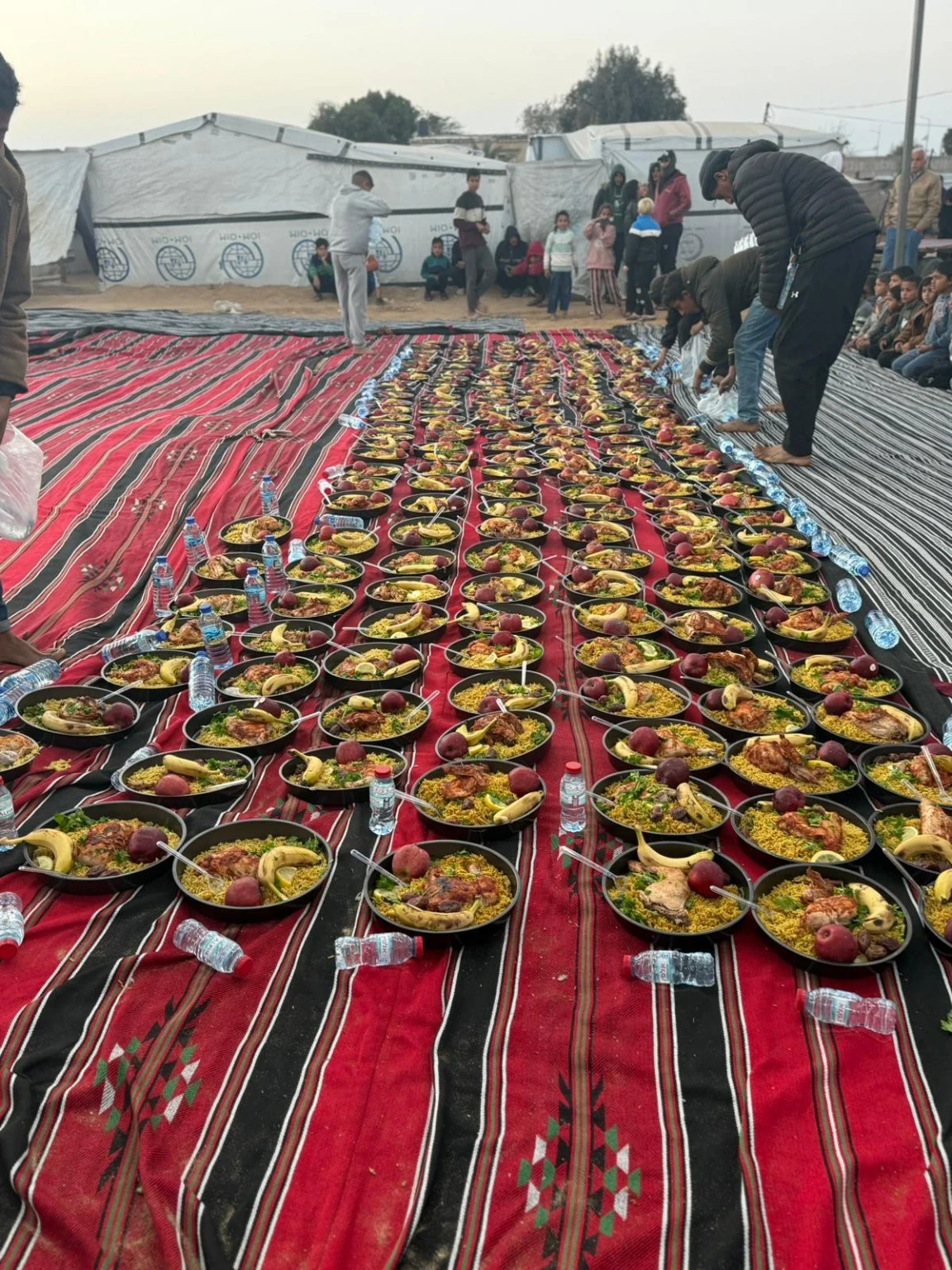 Des assiettes de repas sont disposées sur des tapis dans un camp